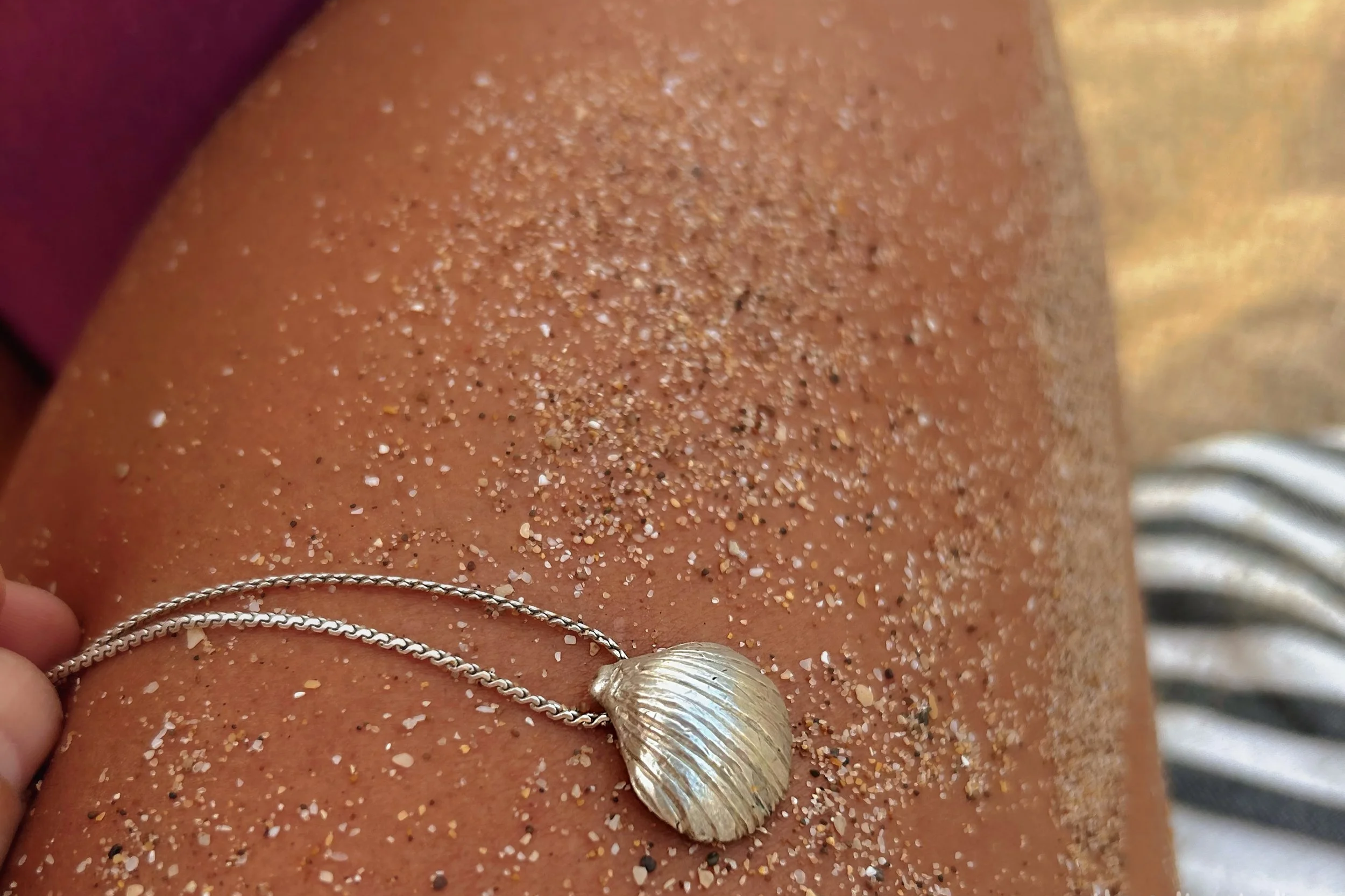 A silver shell-shaped necklace resting on sandy skin.