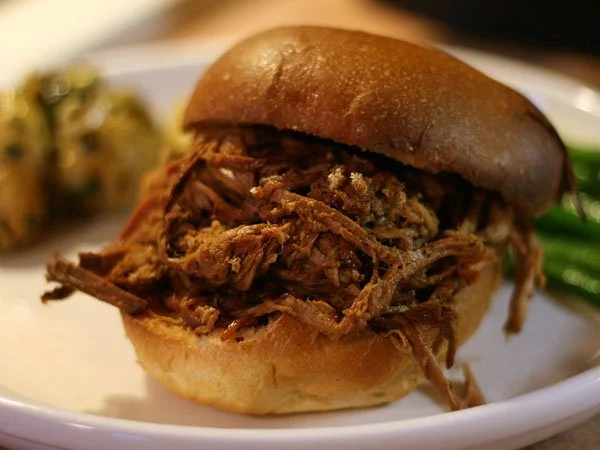 Pulled pork sandwich in a bun with side greens
