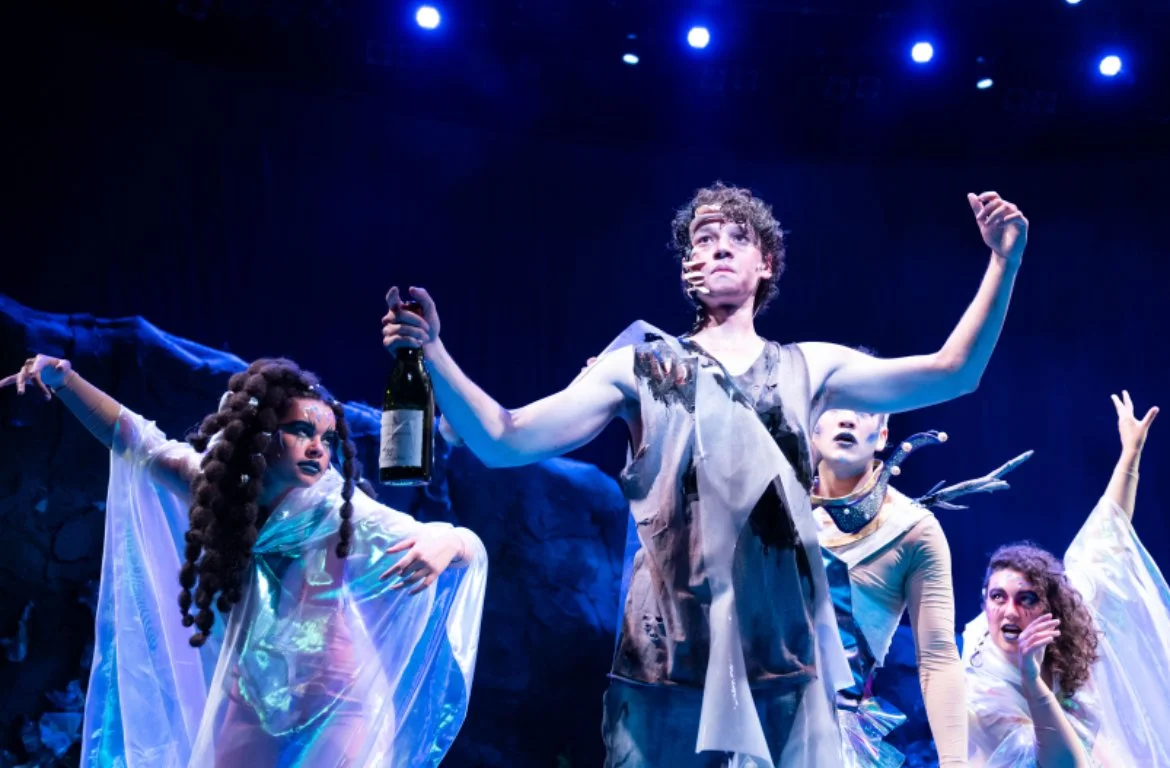Group of actors performing on stage in a theatrical play, with dramatic lighting and fantasy costumes.