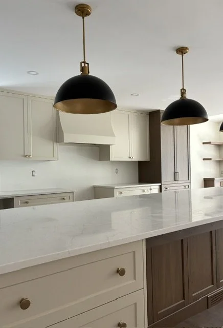 Modern kitchen with white cabinets, a marble island, and two black and gold pendant lights hanging from the ceiling.