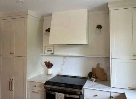 Kitchen with white cabinets, a white range hood over a stove, and decorative items on the countertops and wall.