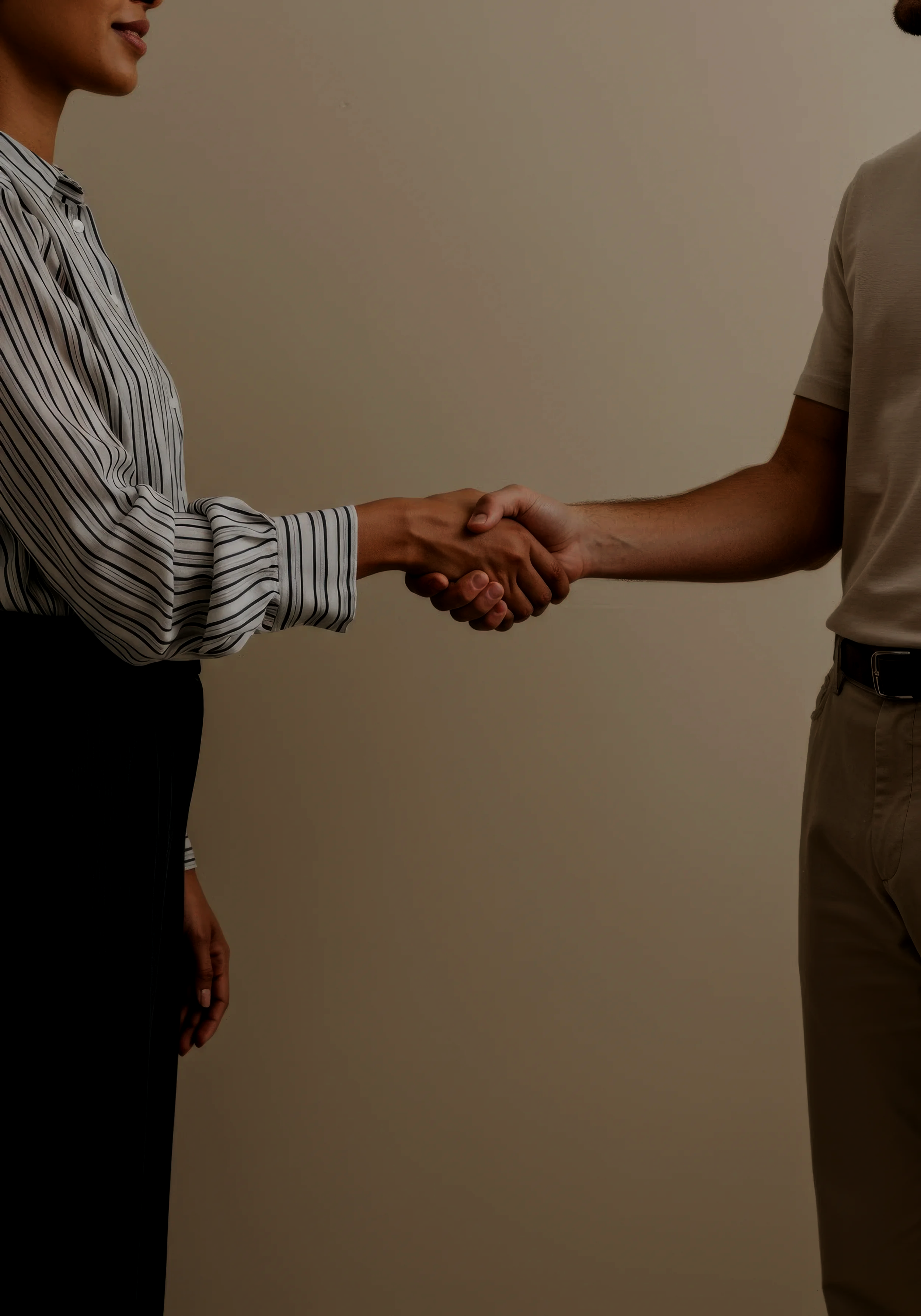 A close-up of two people shaking hands inside, one person wearing a striped shirt and the other in a beige shirt.