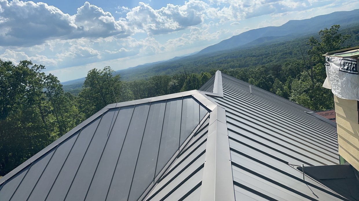 Metal roofs on buildings with a background of green trees, mountains, and a partly cloudy sky.