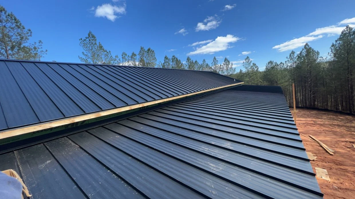 Metal roofing panels on a sloped roof, with blue sky and trees in the background.