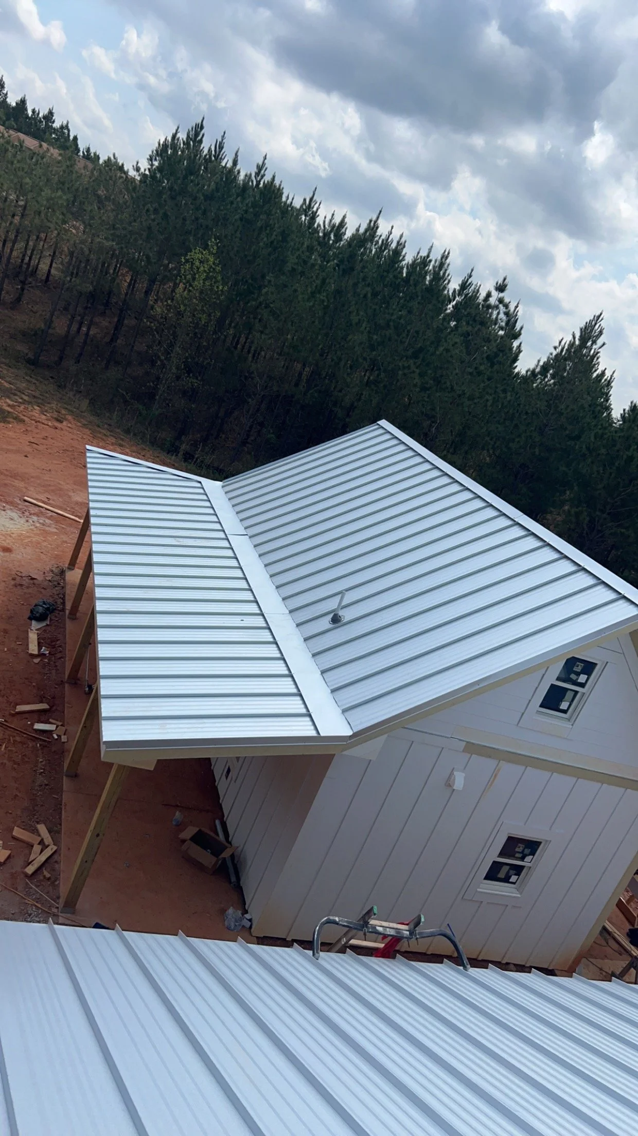 Metal roof on a house under construction, with a cloudy sky and trees in the background.