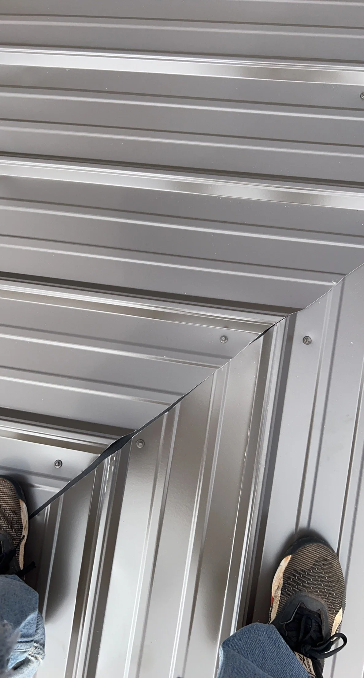 Close-up of a metallic, ribbed surface, likely a metal wall or ceiling panel, with visible screws and the edge of a frame.