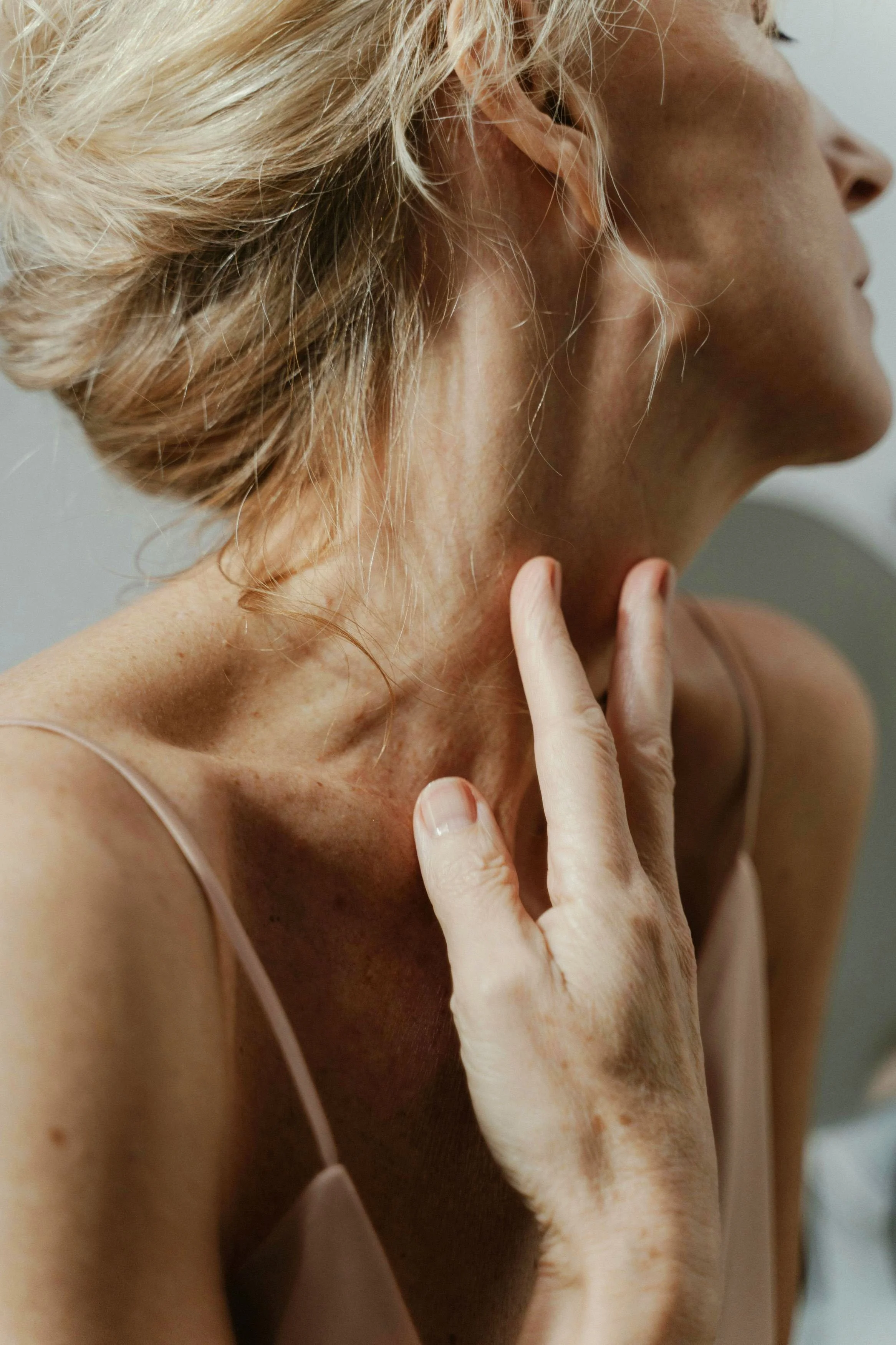 Close-up of a woman with blonde hair touching her neck with her hand.