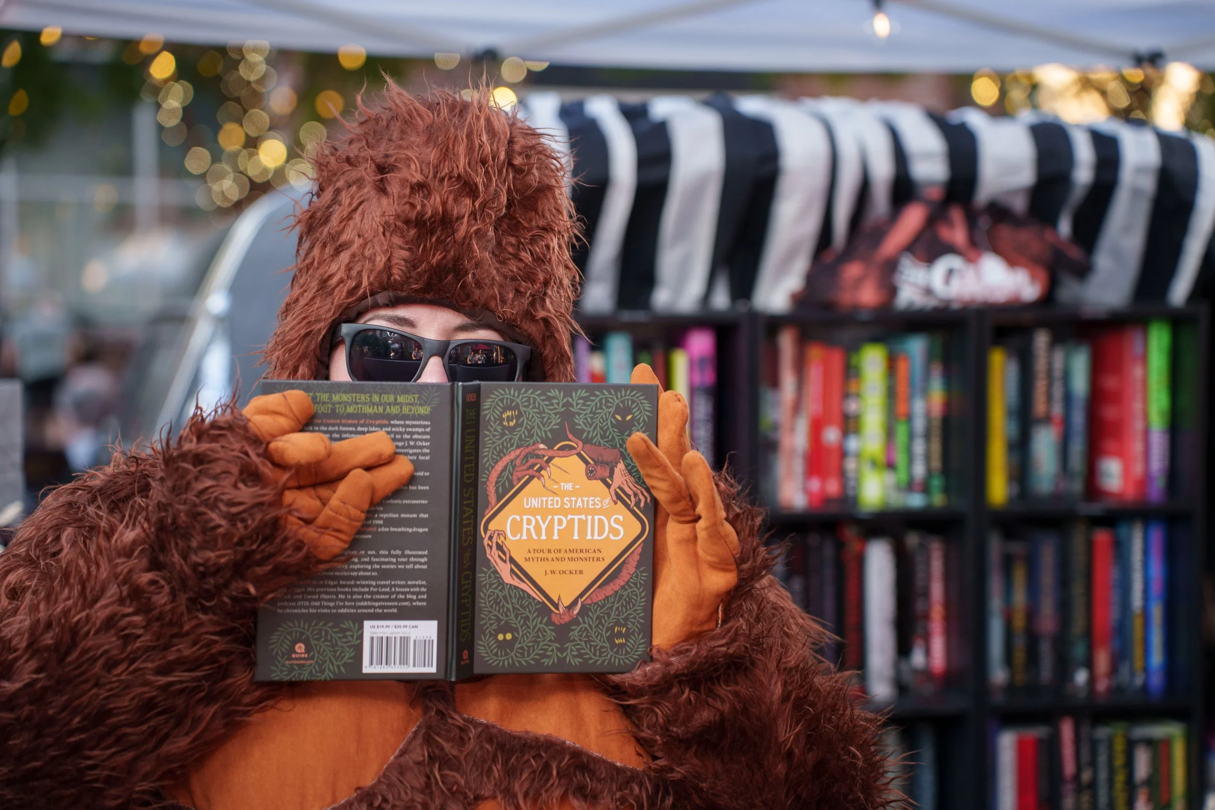 Person wearing a bigfoot costume holding a book titles The United States of Cryptids