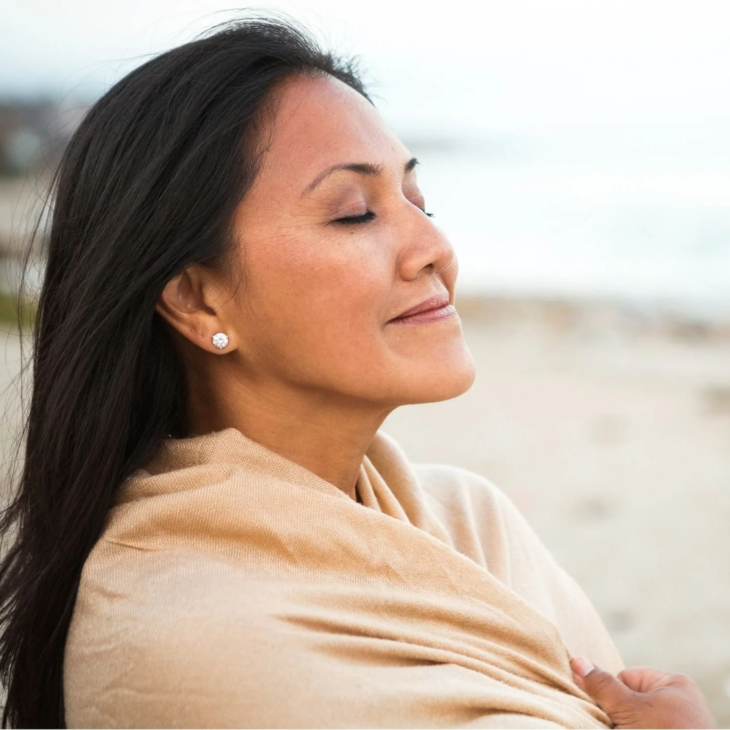 Woman with closed eyes, smiling gently, outside near the beach