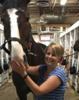 A woman smiling and holding a horse's face in a stable.