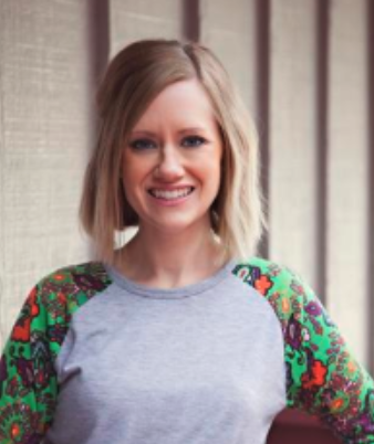 Smiling woman with shoulder-length blonde hair wearing a gray shirt with colorful floral patterned sleeves