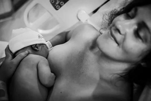 A woman holding a newborn baby against her chest in a hospital setting.