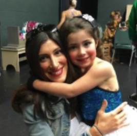 A woman and a young girl are hugging and smiling in a room decorated for a celebration, possibly a birthday party.