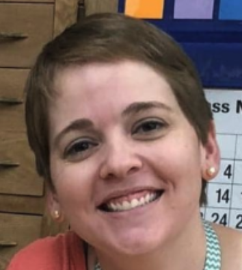 Close-up of a smiling woman with short brown hair and earrings, indoors with a wooden and blue background.