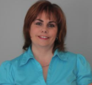 A woman with shoulder-length reddish brown hair wearing a light blue button-up shirt, smiling at the camera.