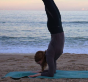 Person practicing downward-facing dog yoga pose on the beach at sunset.
