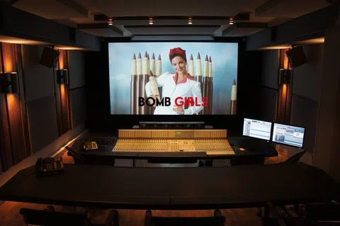 Recording studio control room with two monitors and large screen showing a woman with red hair and lipstick, with pencils in the background and the text "BOMB GALS."