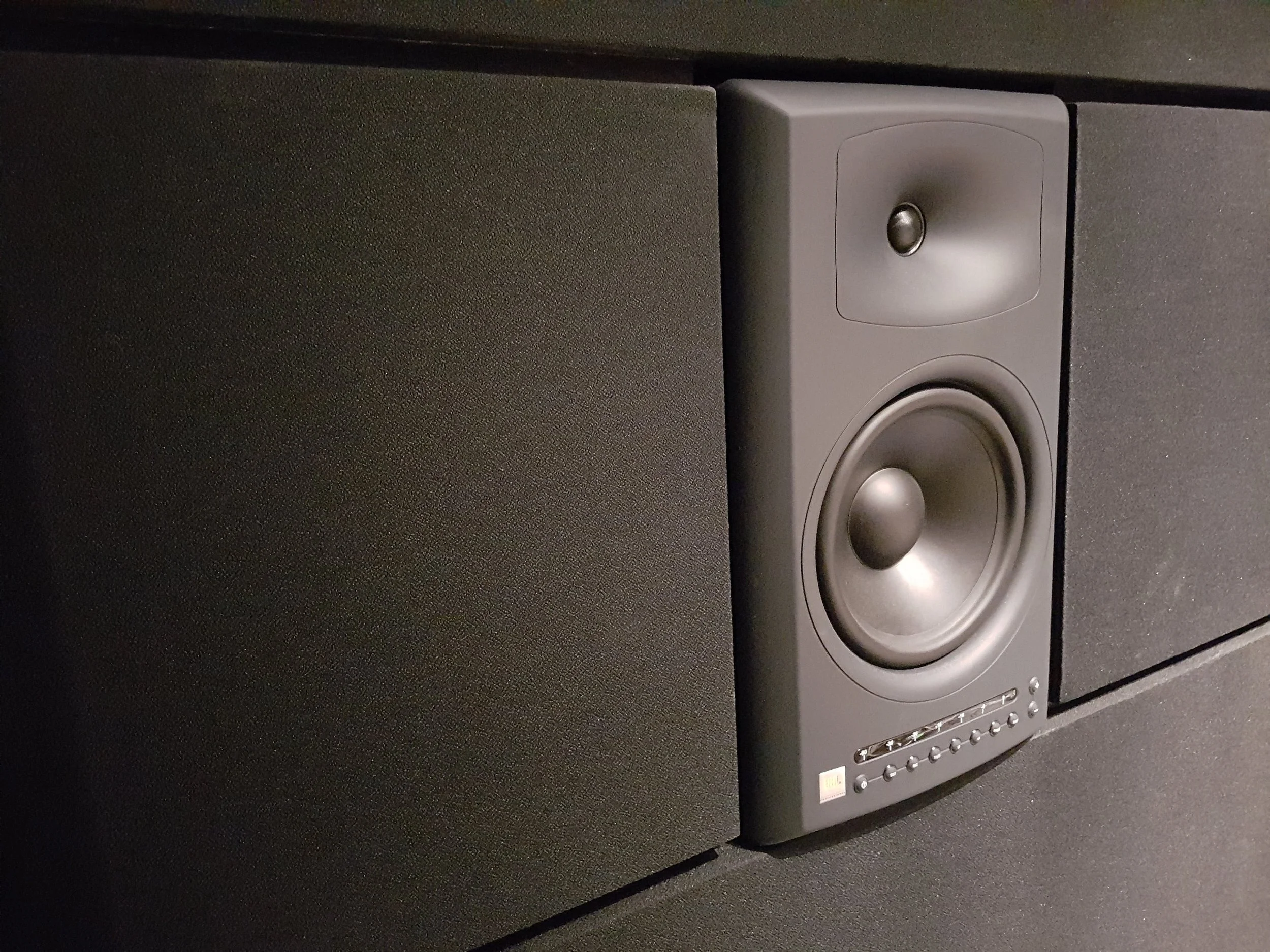 Close-up of a black speaker with a small black tweeter and a larger black woofer, placed in front of a black textured background.