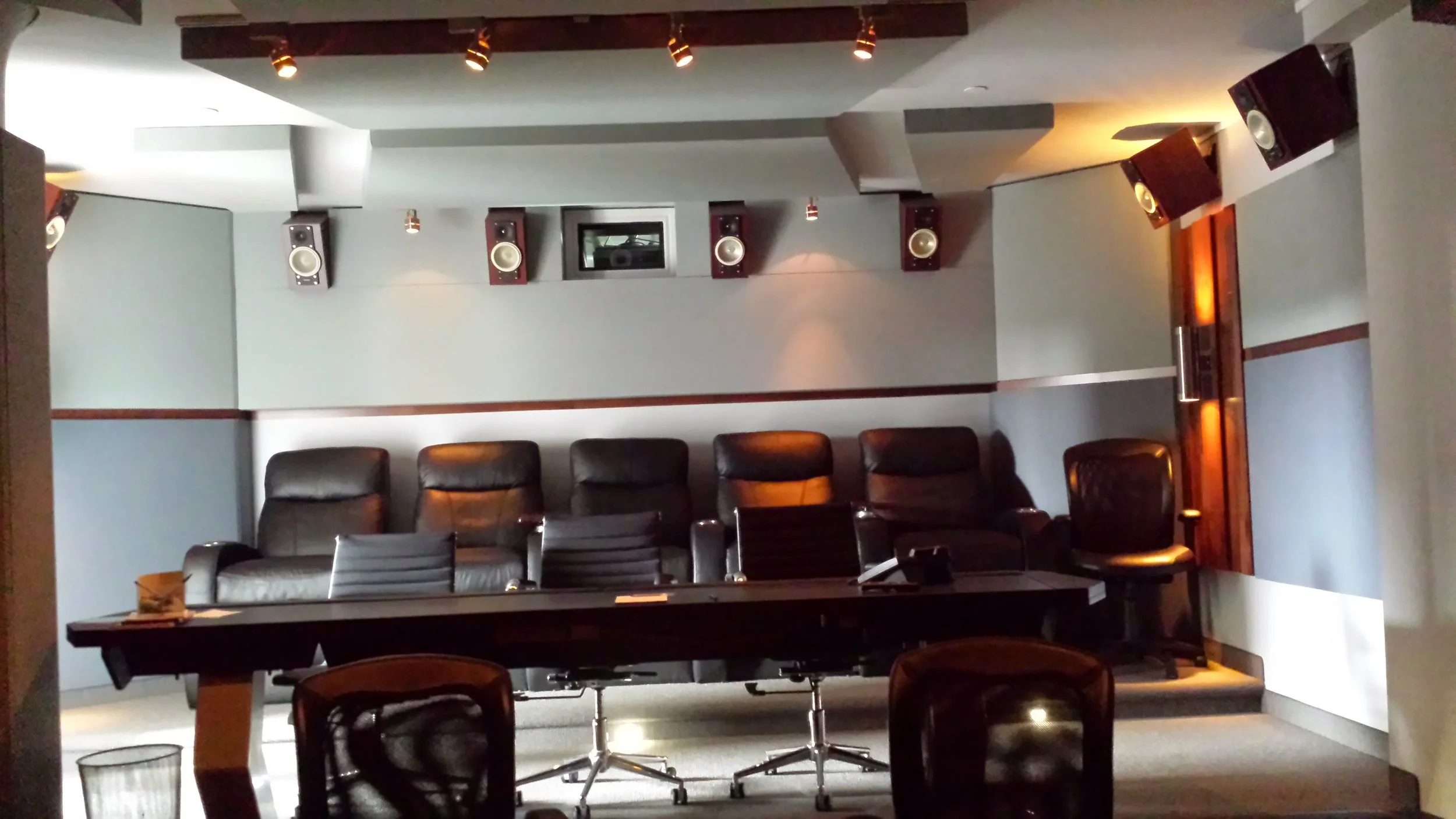 A conference room with six black leather chairs, a long black table, and a wall-mounted audio system with multiple speakers.