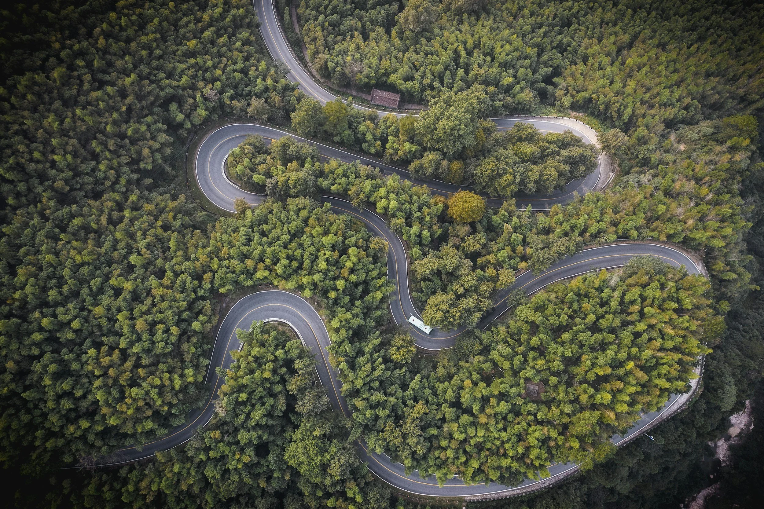 An aerial view of a winding mountain road through a dense green forest.