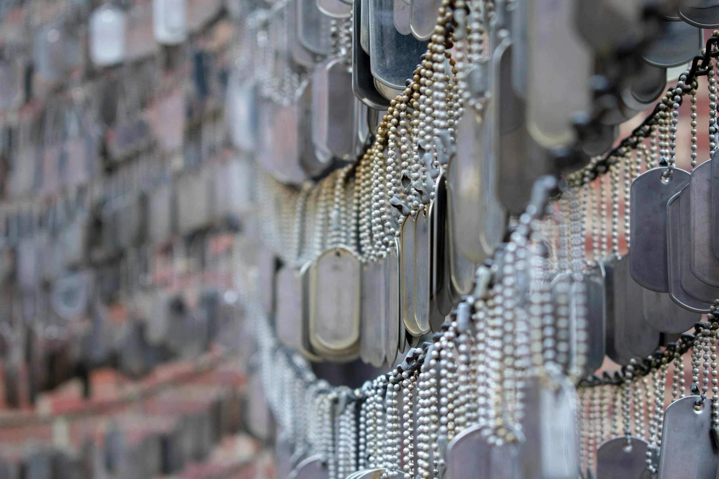 Rows of metal dog tags and beaded chains hanging on a display.