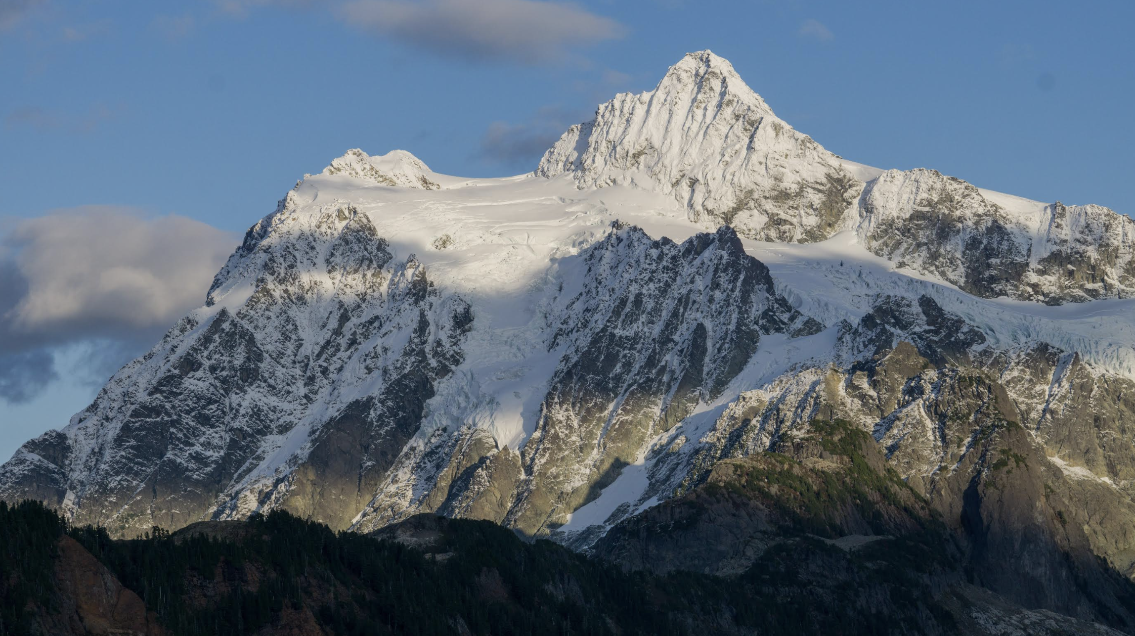 Snow-covered mountain with a sharp peak under a partly cloudy sky.