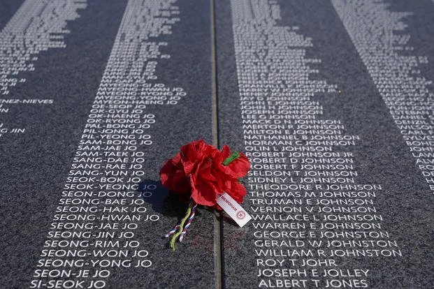 Close-up of a memorial wall with engraved names, a red flower, and a small note, honoring fallen soldiers.