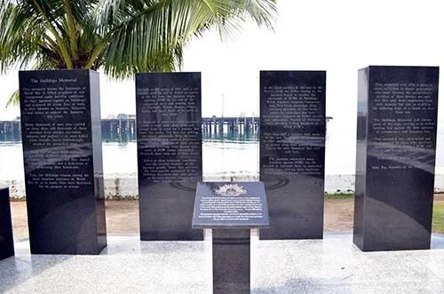 Hellships  memorial with five black stone plaques with engraved text, set outdoors near Subic Bay and palm trees.