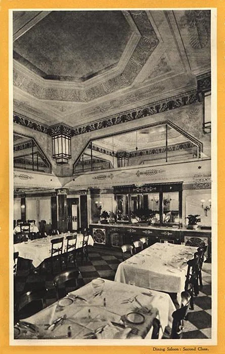 Historic dining room with tables set for service, ornate ceiling, and decorative wall trim.