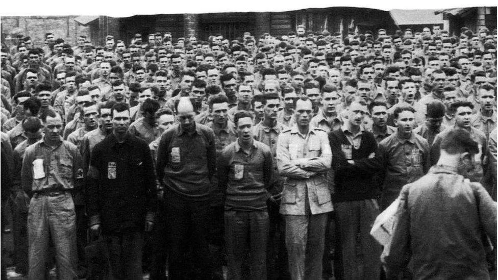Black and white photograph of a large group of men standing outdoors, facing forward, with some wearing uniforms and others in civilian clothing.