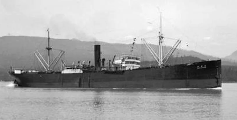 A black-and-white photo of a large early 20th-century cargo or passenger ship on calm water with mountains in the background.