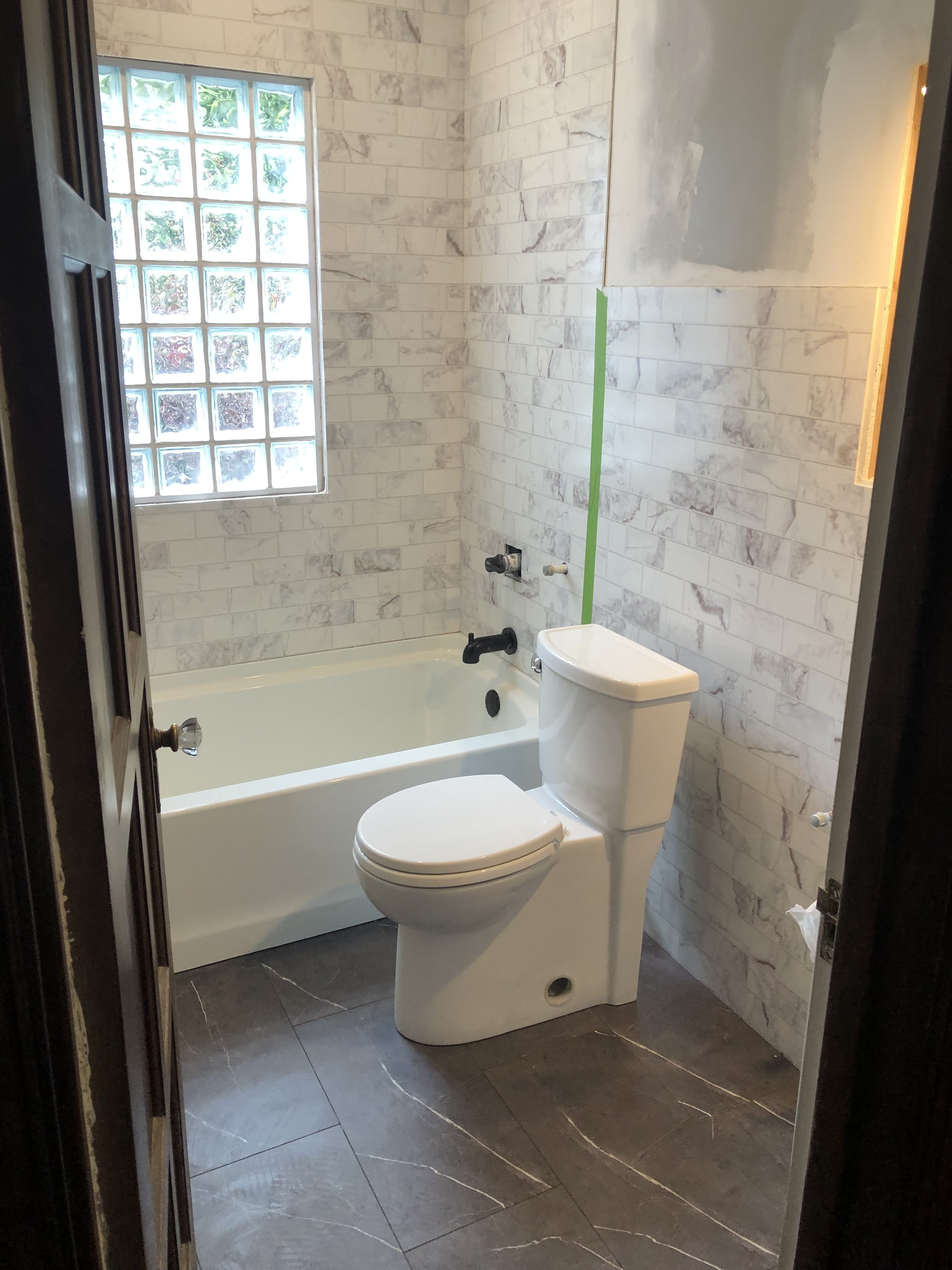Bathroom remodel in progress featuring new tile surround, tub installation, and modern toilet.