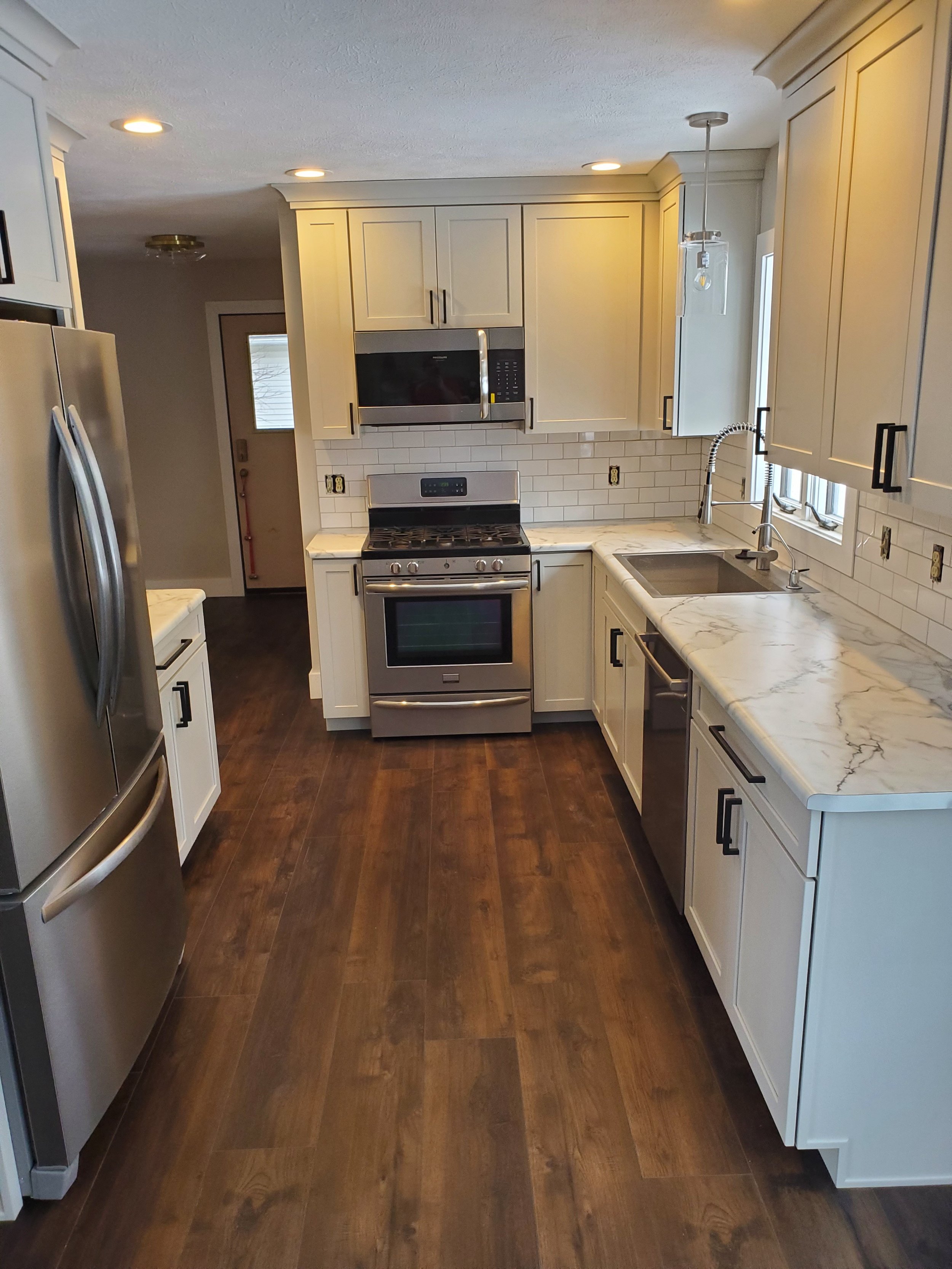Modern kitchen remodel featuring white shaker cabinets, gray countertops, stainless steel appliances, and wood-look vinyl flooring.