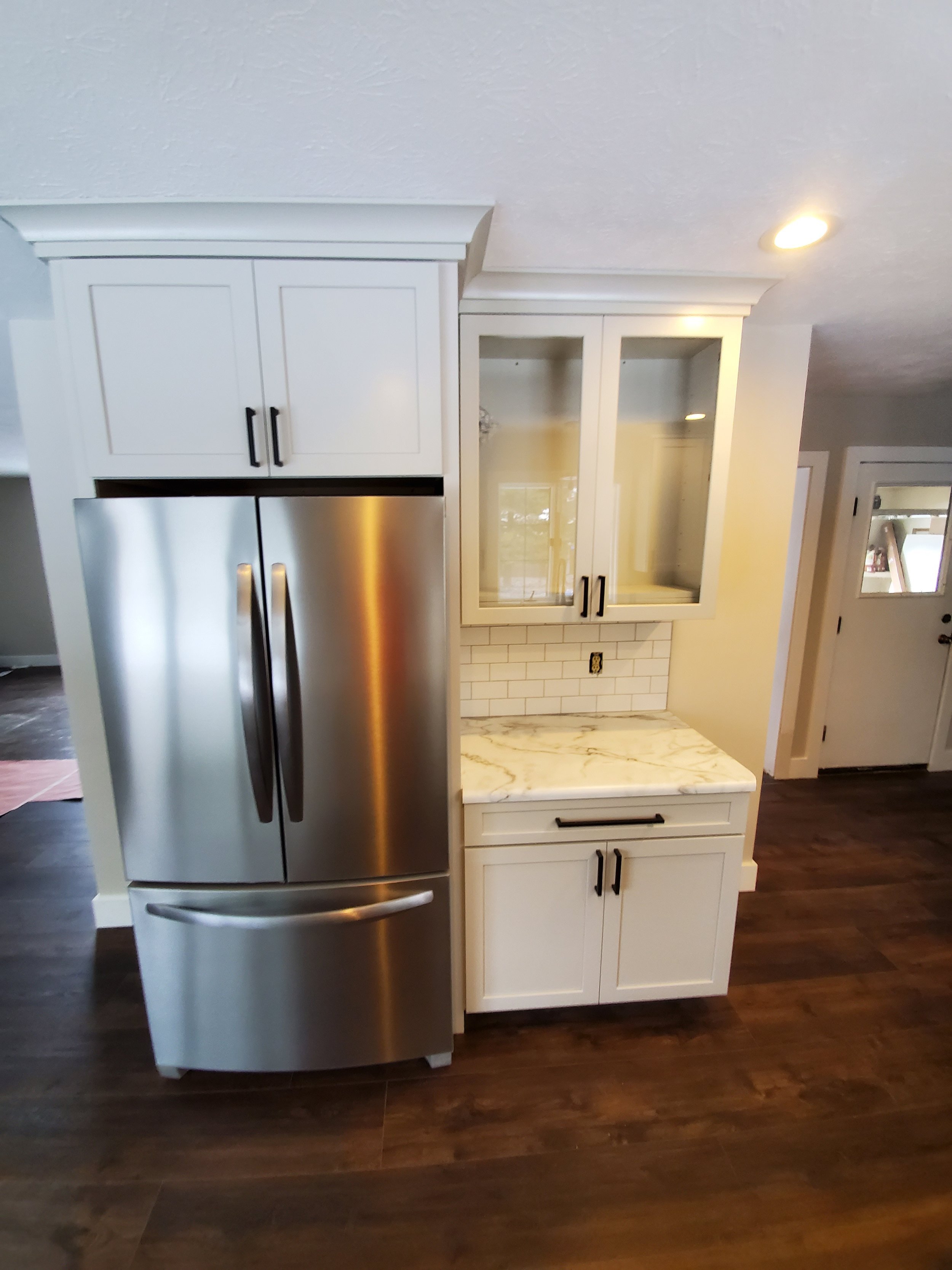 Kitchen remodel with added storage and style, including stainless steel refrigerator and a glass-door upper cabinet above a marble-look countertop.