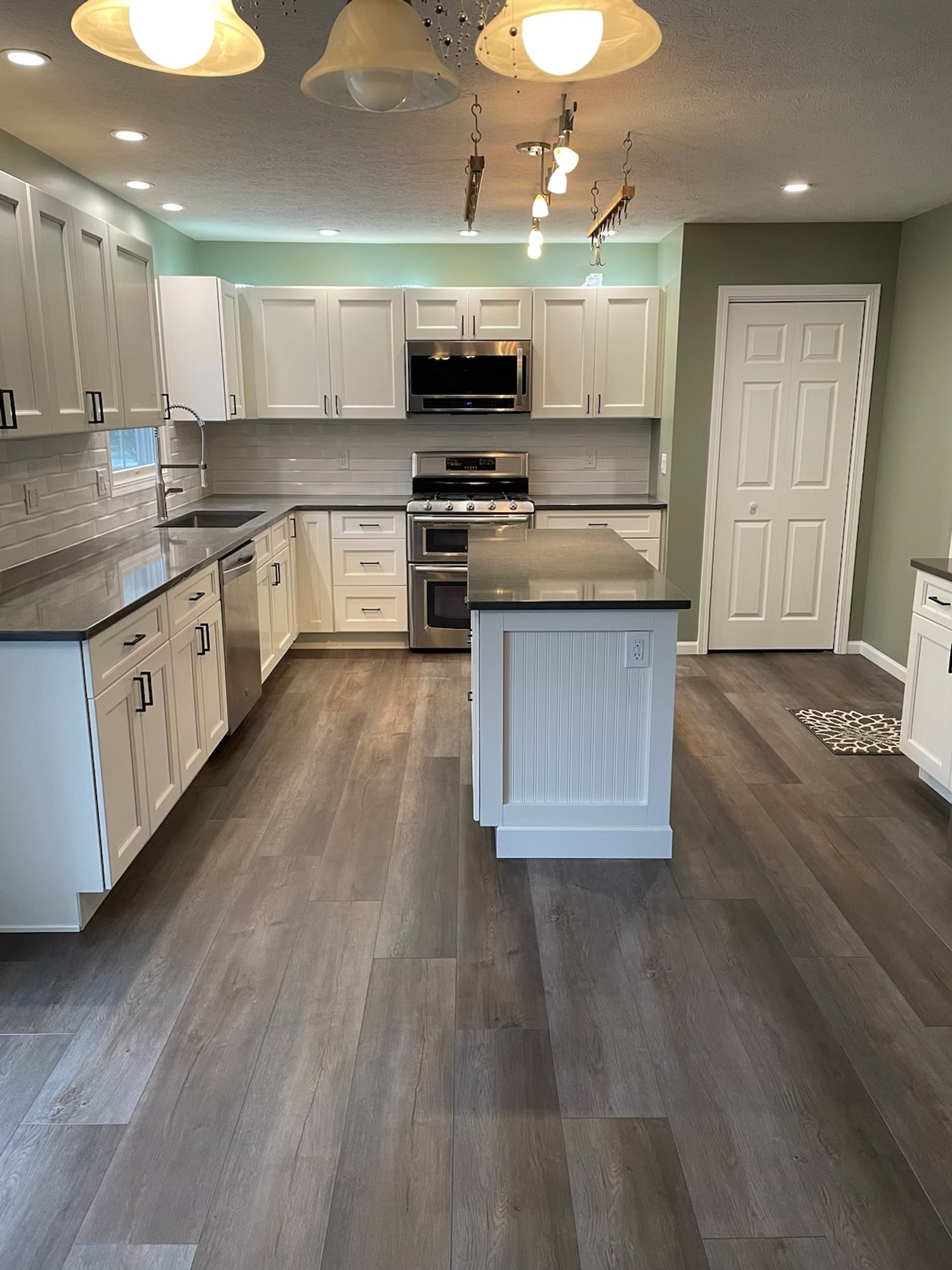 Modern white kitchen remodel with center island, stainless steel range, and gray plank flooring.