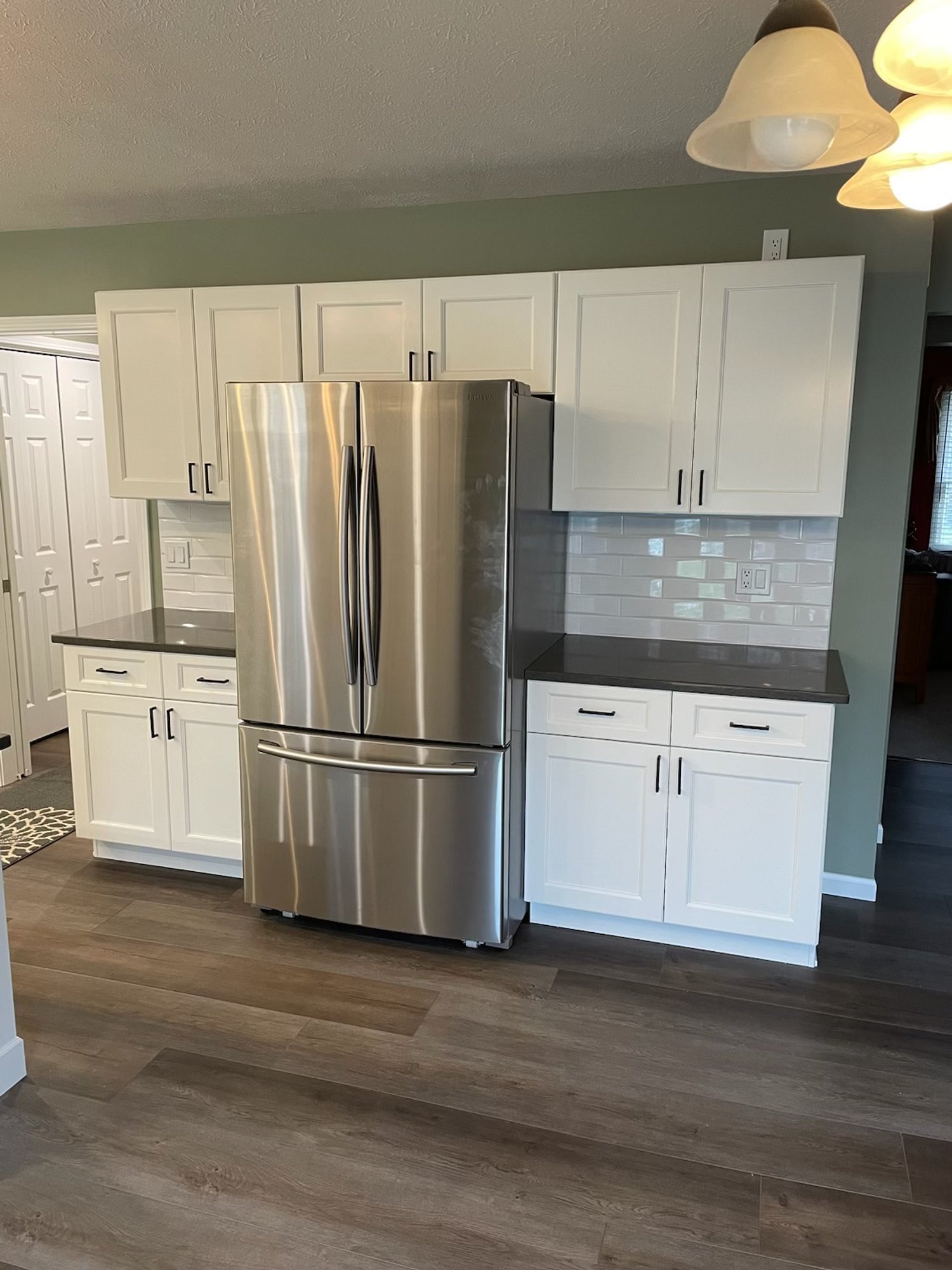 Updated kitchen featuring white shaker cabinets, black countertops, stainless steel French door refrigerator, and subway tile backsplash.