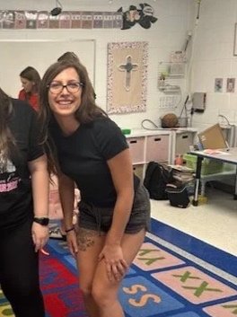A young woman with long brown hair, wearing a white shirt, smiling at the camera against a plain background.