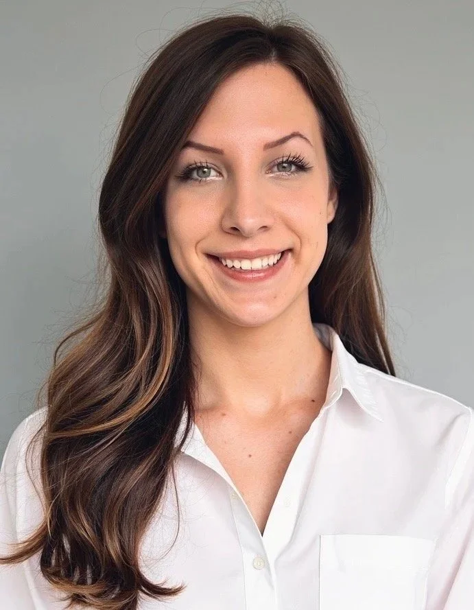A young woman with long brown hair, wearing a white shirt, smiling at the camera against a plain background.