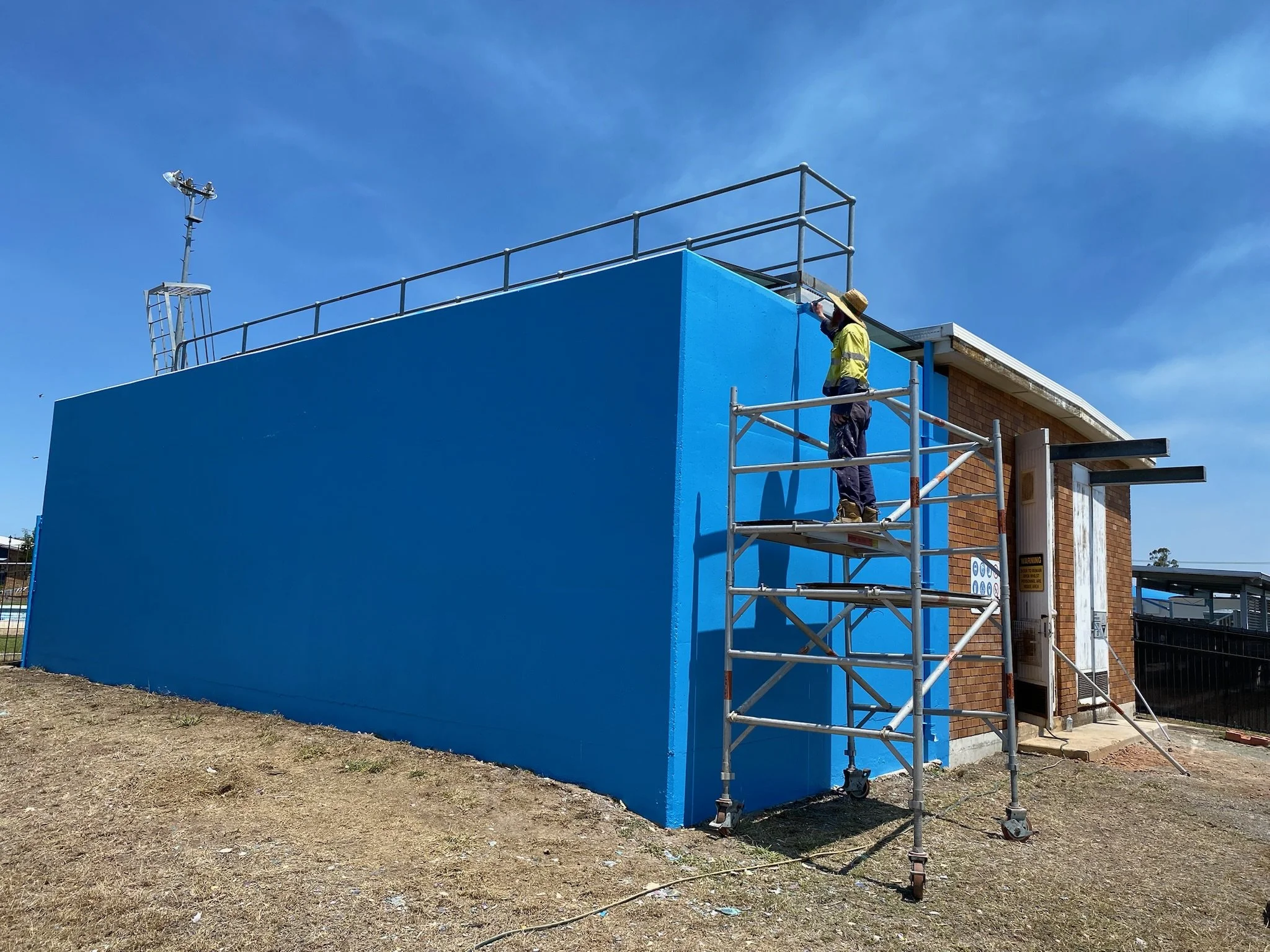 Coast2Country Linemarking & Painting team painting a Commercial Property in Gladstone bright blue in order to cover graffiti that had occurred over many years