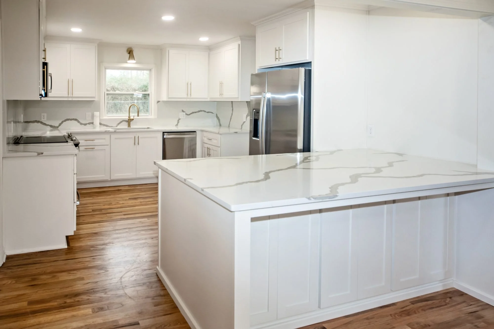 Remodeled white kitchen with shaker cabinets, quartz countertops and a center island