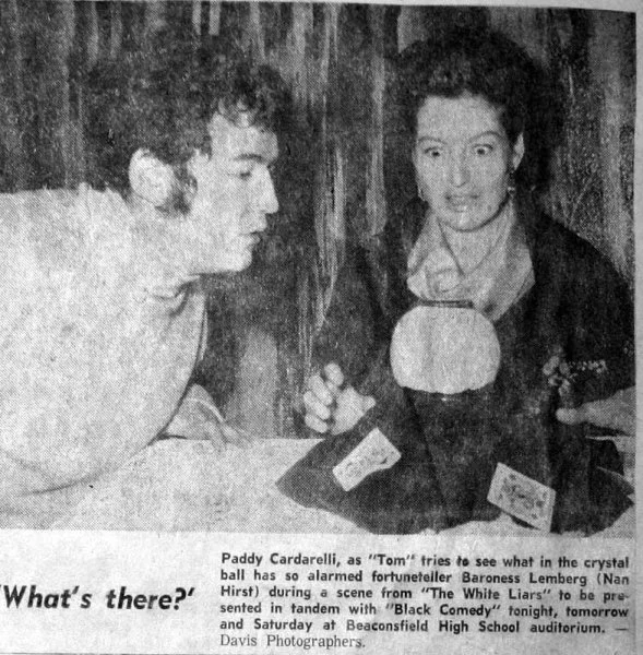 Two women sitting at a table having a conversation. One woman is holding a microphone towards the other.