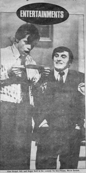 Black-and-white photo of two men, one standing and one sitting, smiling. The standing man is holding a newspaper or magazine. They appear to be in a comedic scene related to entertainment.