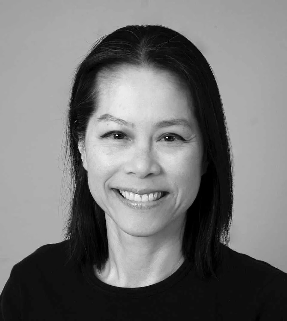 A black and white photo of a smiling woman with shoulder-length dark hair, wearing a dark top, against a plain background.