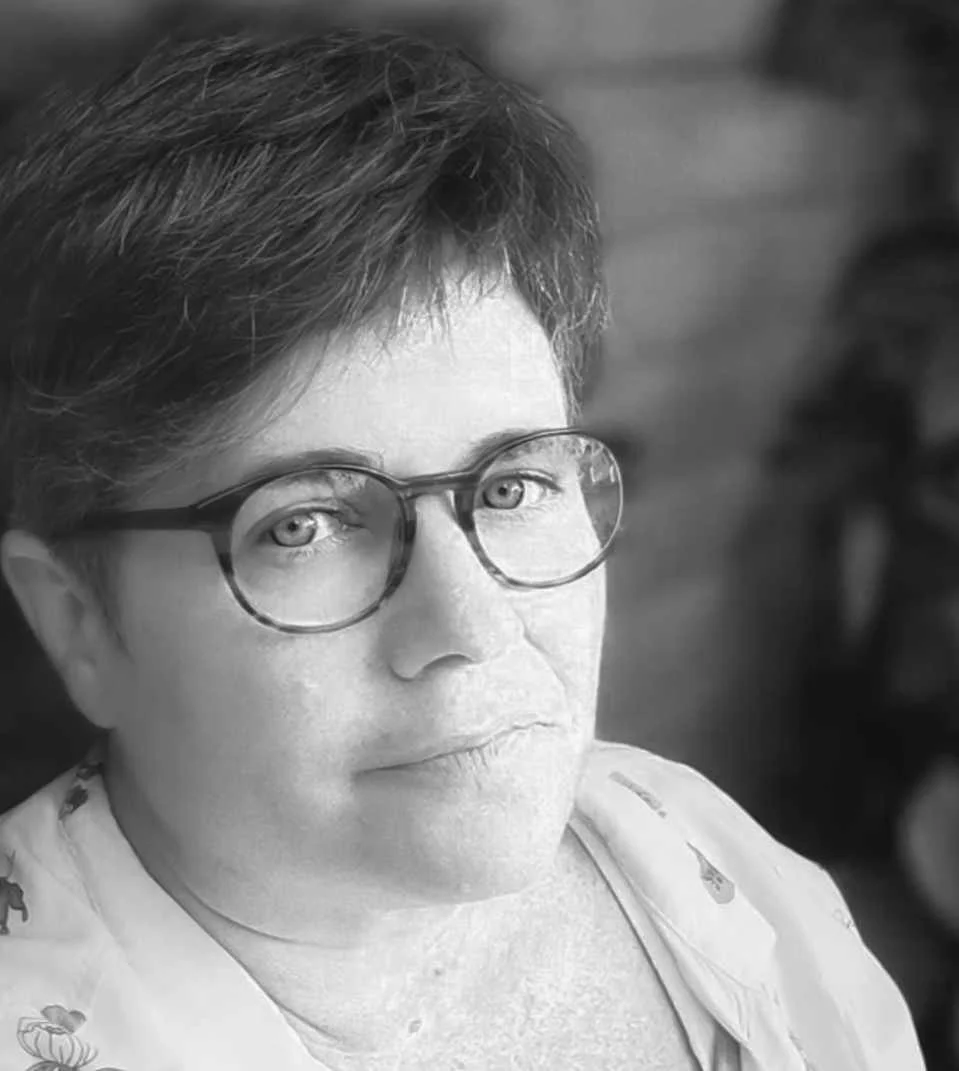 Black and white photo of a woman with short hair and glasses, looking directly at the camera with a serious expression.
