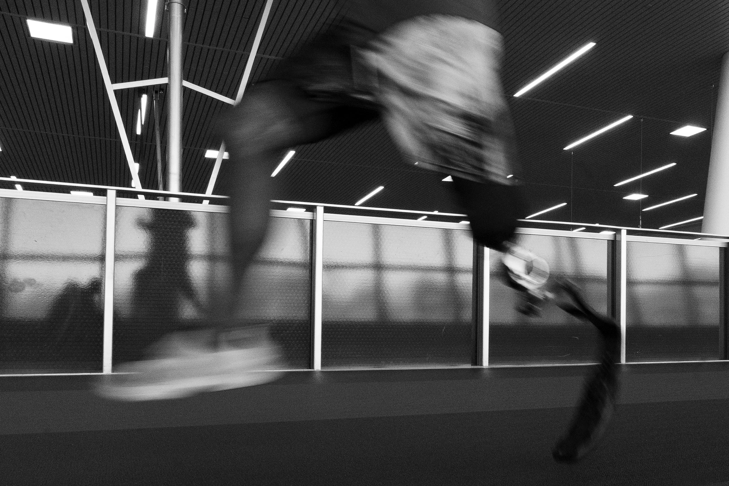 A person in motion running indoors, captured with motion blur, in a modern building with sleek lighting and metal railings.