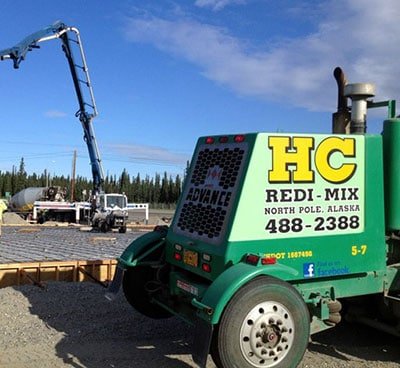 Construction site with a green concrete pump truck, steel reinforcement bars, and a blue sky with clouds.