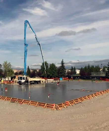 Construction site with concrete being poured into a large foundation.