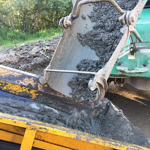 A construction site where a dump truck is unloading wet concrete into a yellow container.