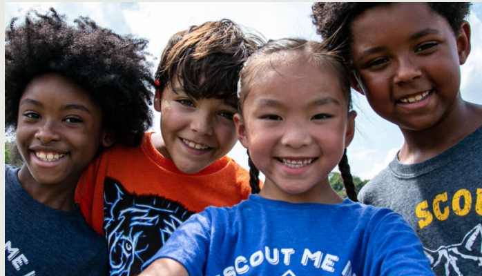 Group of five smiling children taking a selfie outdoors.