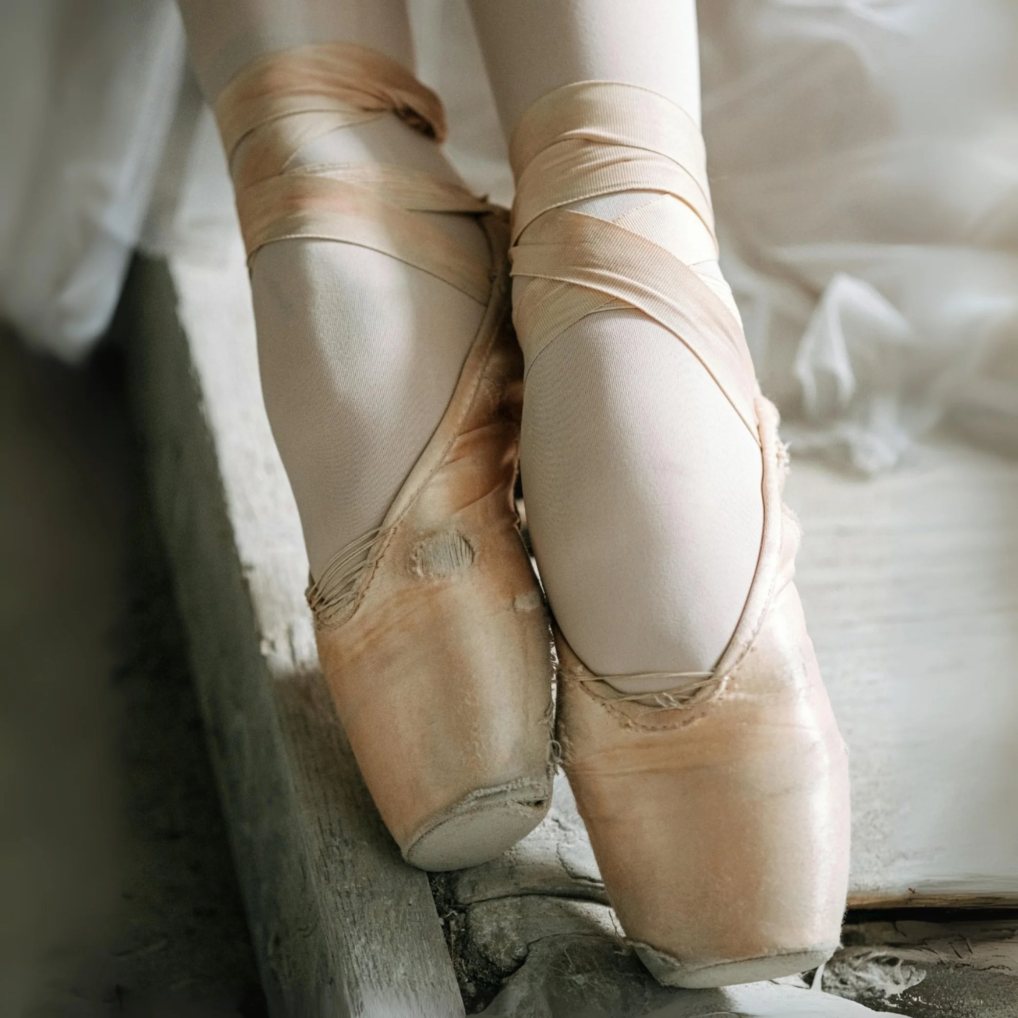 Close-up of worn ballet pointe shoes with satin ribbons, resting on a wooden surface.